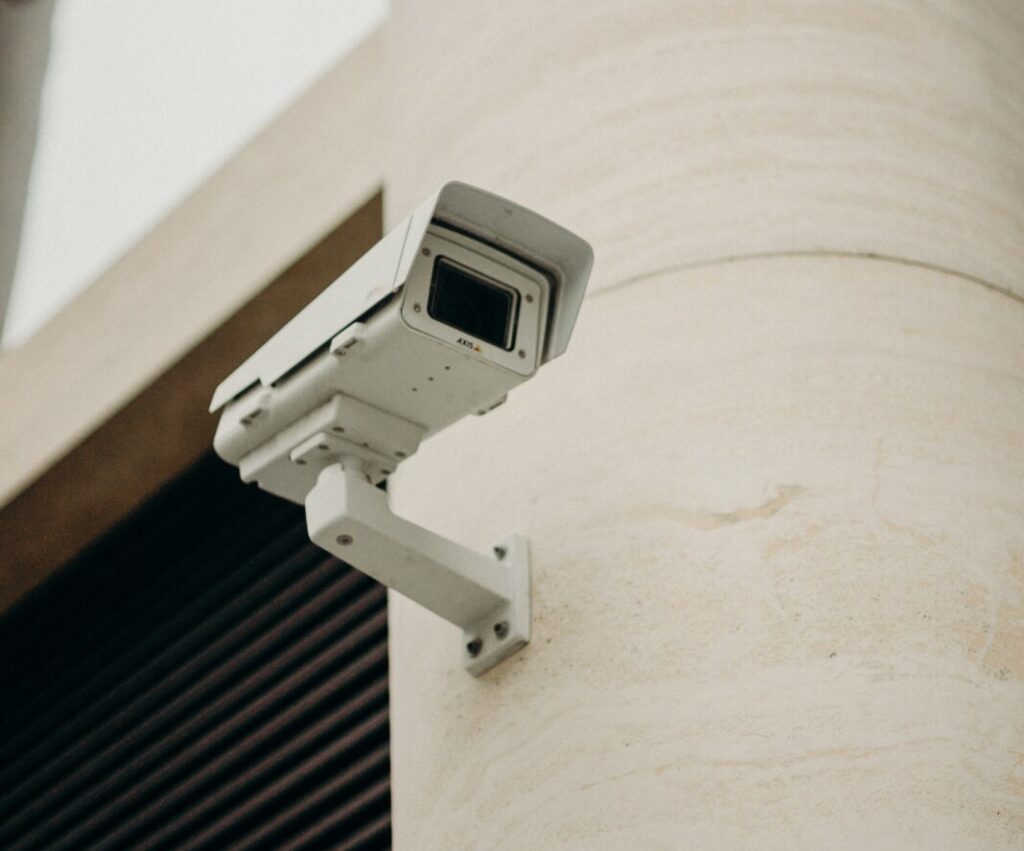 A white CCTV camera mounted onto the outside of a white building.
